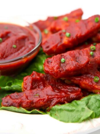 A plate full of tempeh with vegan BBQ sauce on in served on a bed of lettuce.