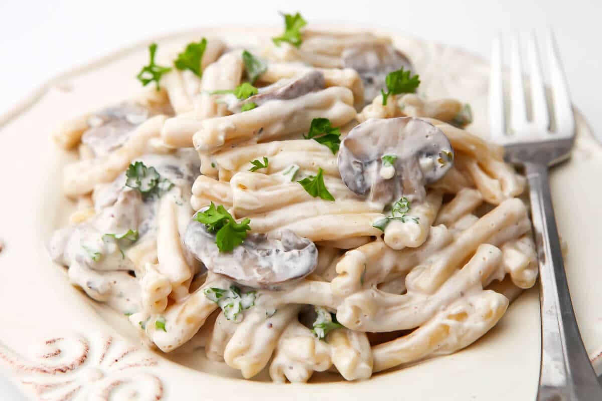 A white plate filled with cream mushroom pasta with a fork on the side.