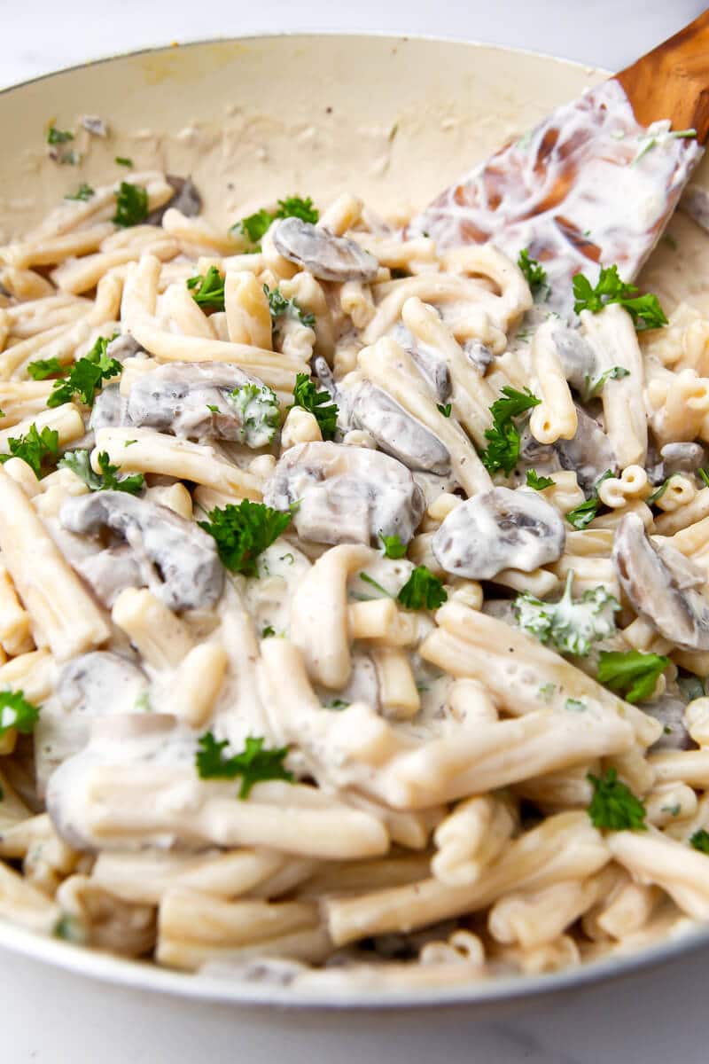 A creamy mushroom pasta in a large wok being stirred with a wooden spoon.