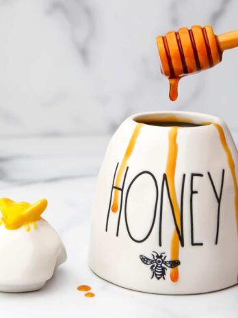A white honey pot filled with vegan honey with some dripping down the sides.