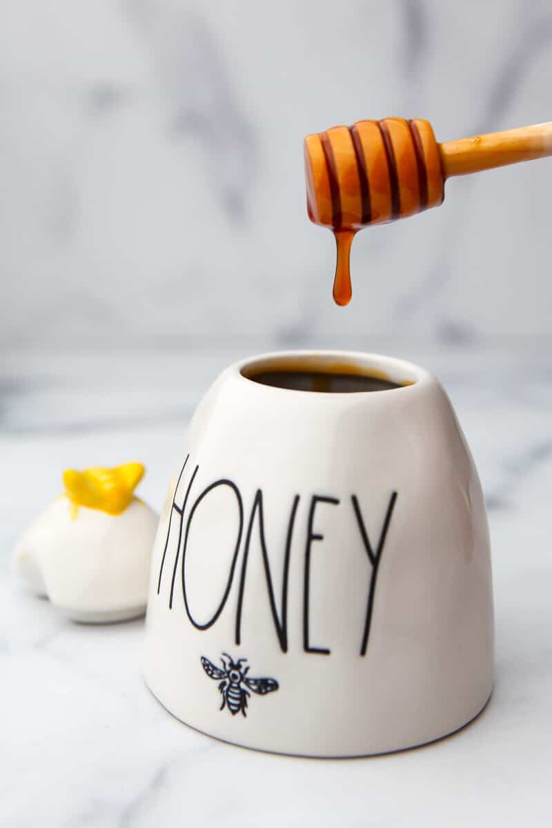 A honey pot with vegan honey dripping off a honey stick.
