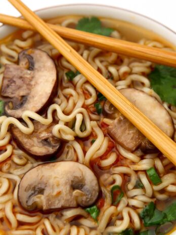 A close up top view of a bowl of vegan ramen with mushrooms and herbs on top.