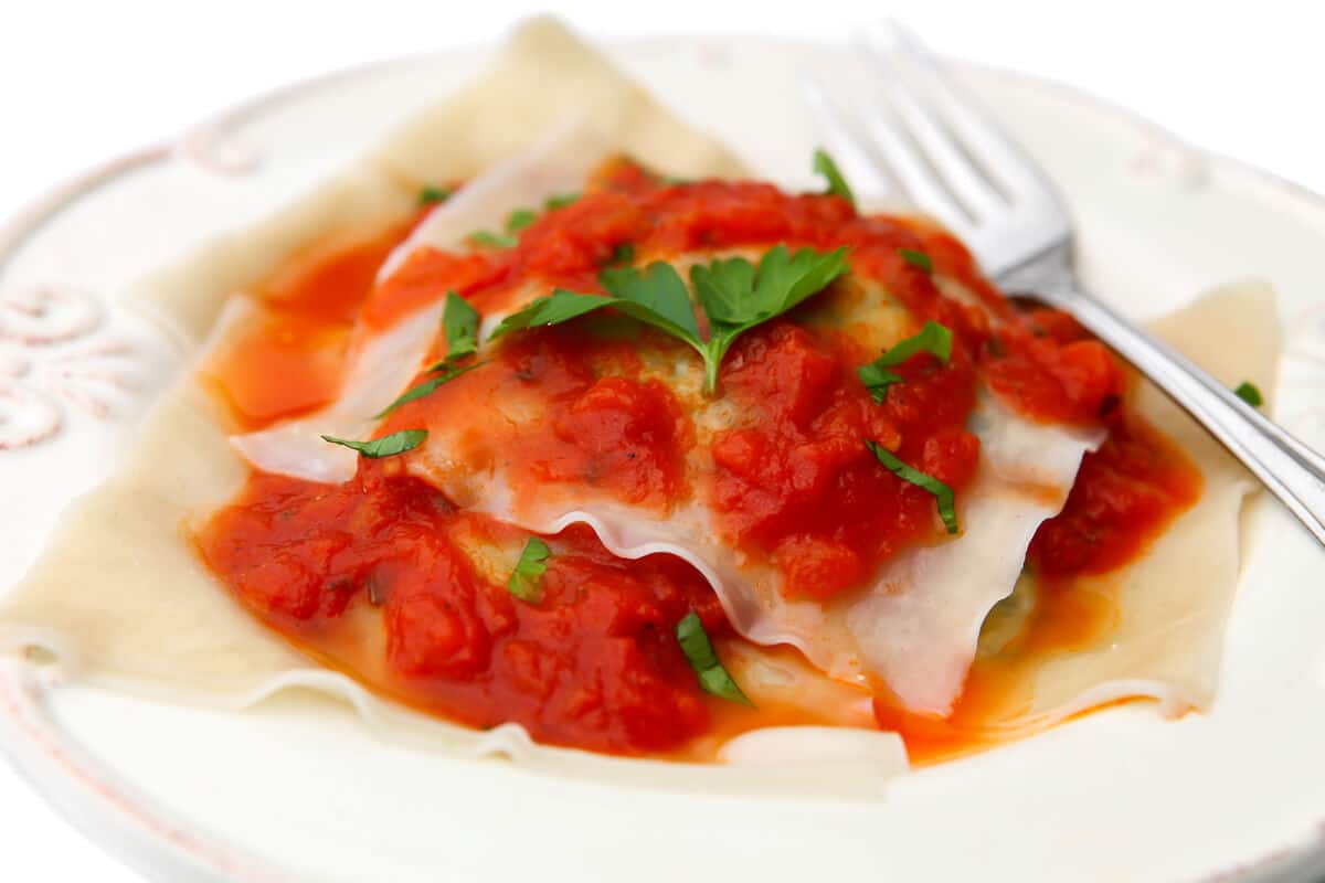 A plate full of vegan ravioli with marinara sauce on top and a fork on the side.