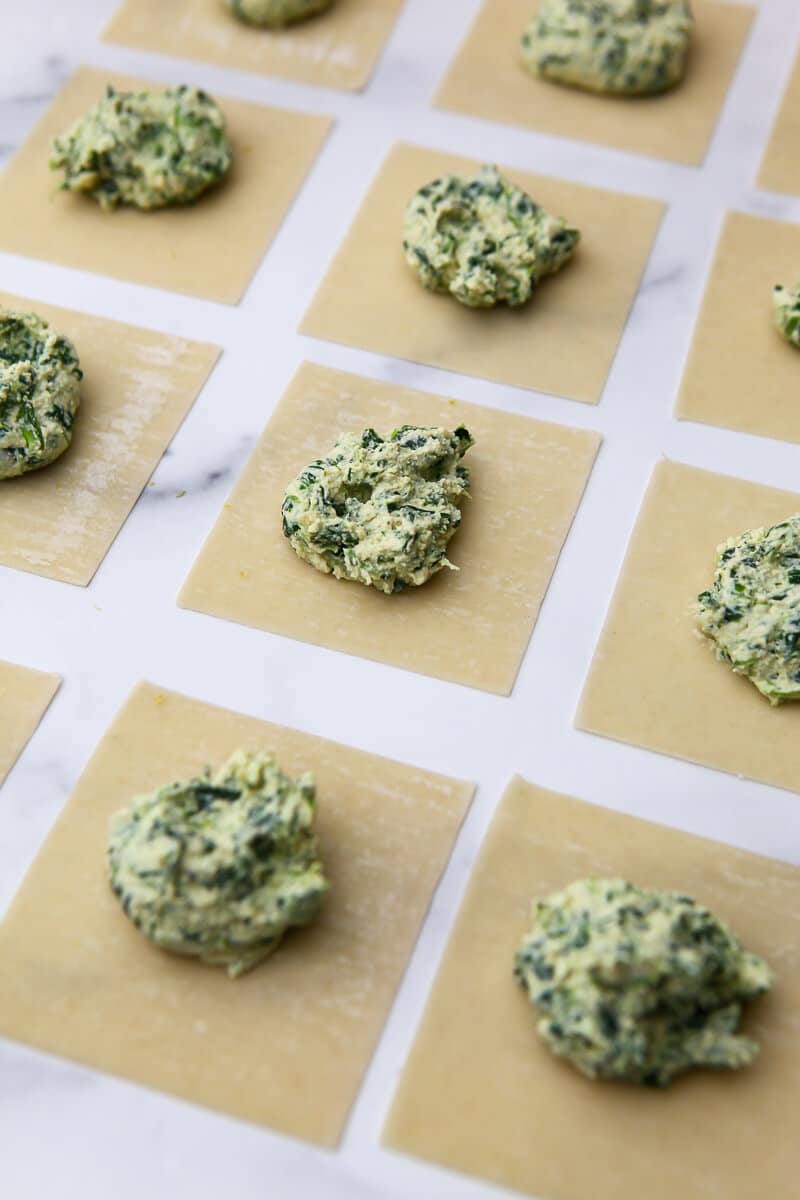 Showing the process of making vegan ravioli by putting a dollop of tofu spinach ricotta in the center of a wonton wrapper.