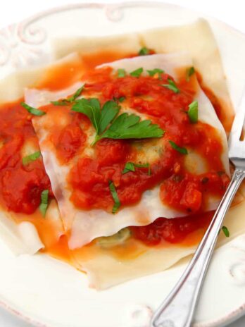 Vegan ravioli on a white plate with red sauce on top and a fork on the side.