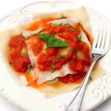 Vegan ravioli on a white plate with red sauce on top and a fork on the side.
