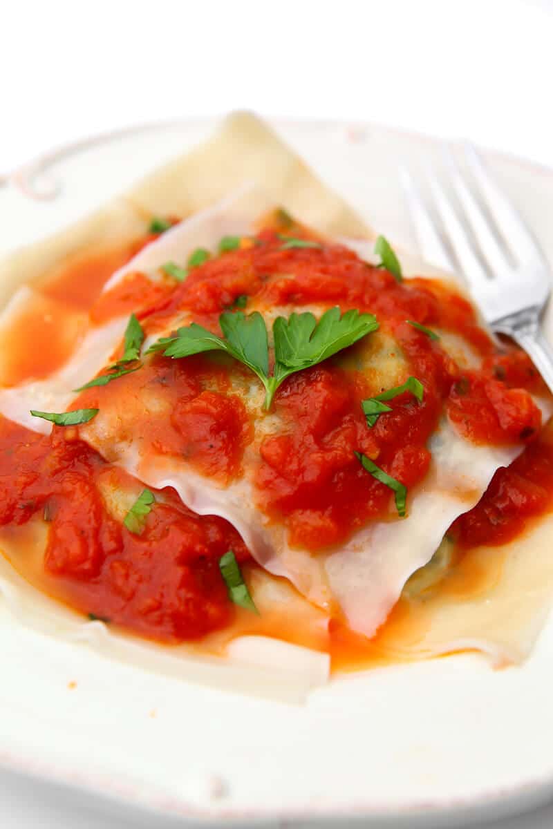A white plate filled with tofu spinach ravioli with red sauce on top.