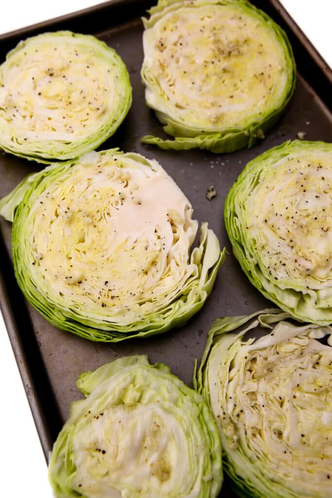 Slices of cabbage on a cookie sheet drizzled with garlic and oil.