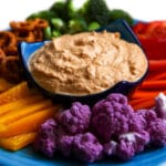 A blue plate filled with colorful veggies with cashew cheese dip in the center.