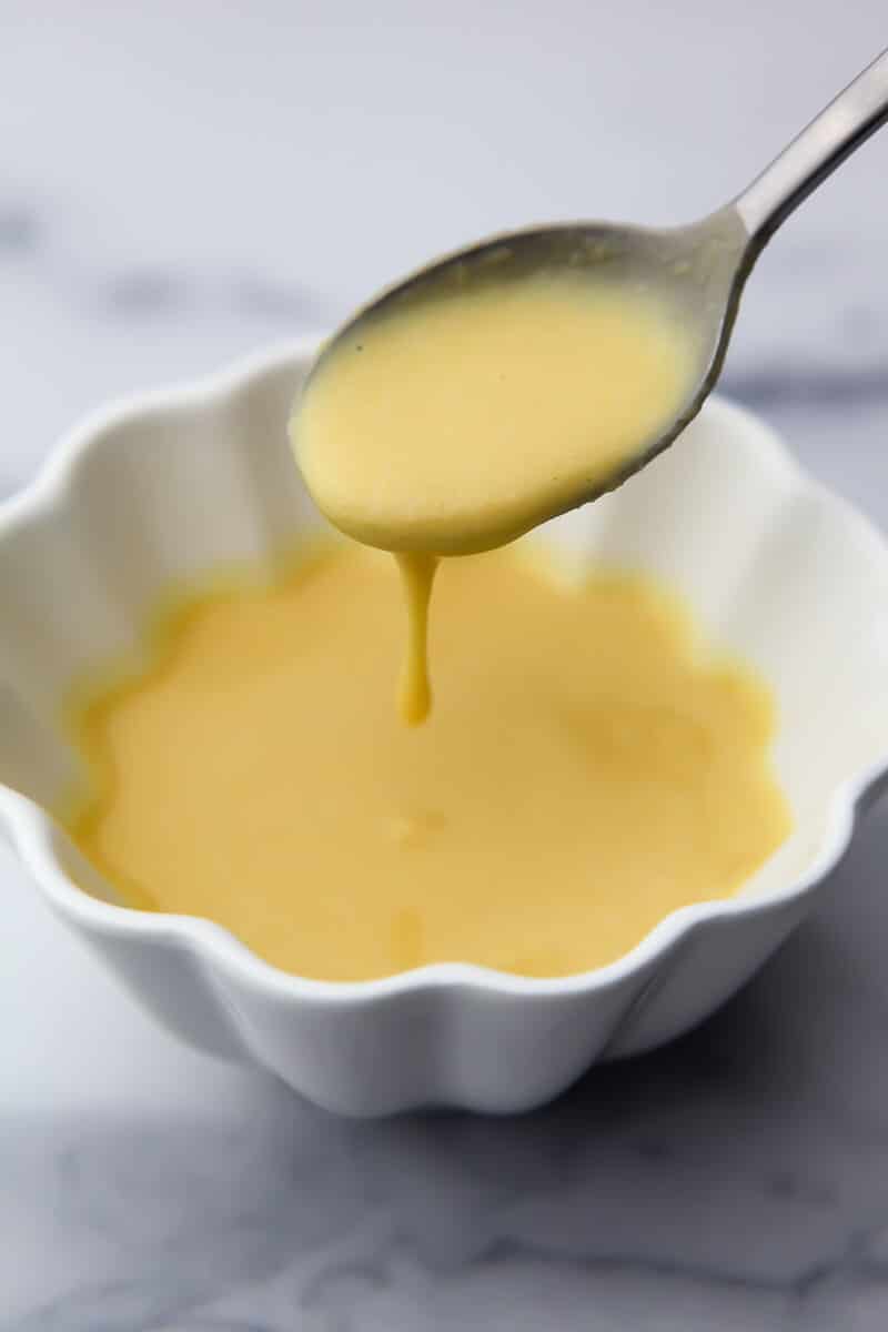 A small white bowl filled with a chickpea flour egg with a spoon dripping some off into the bowl.