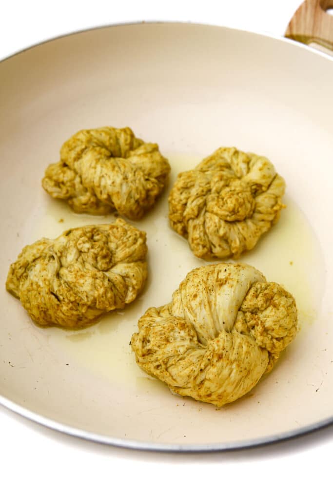 Knots of flour and water chicken frying in oil in a white frying pan.