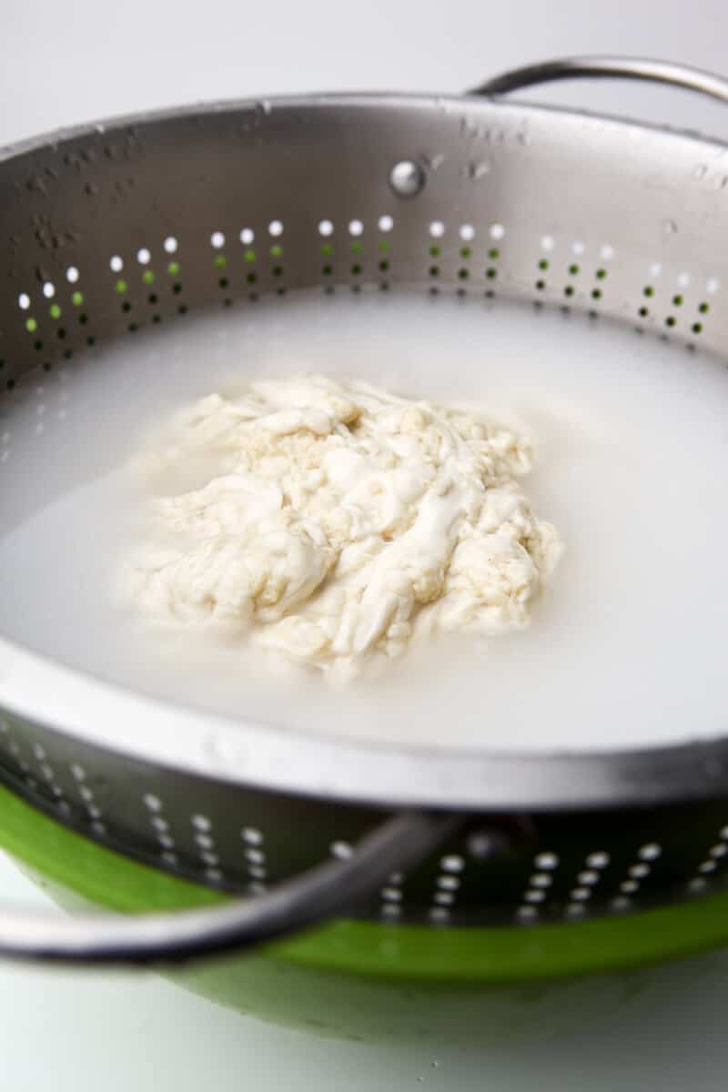 A bowl lined with a strainer filled with water to wash flour to make seitan.