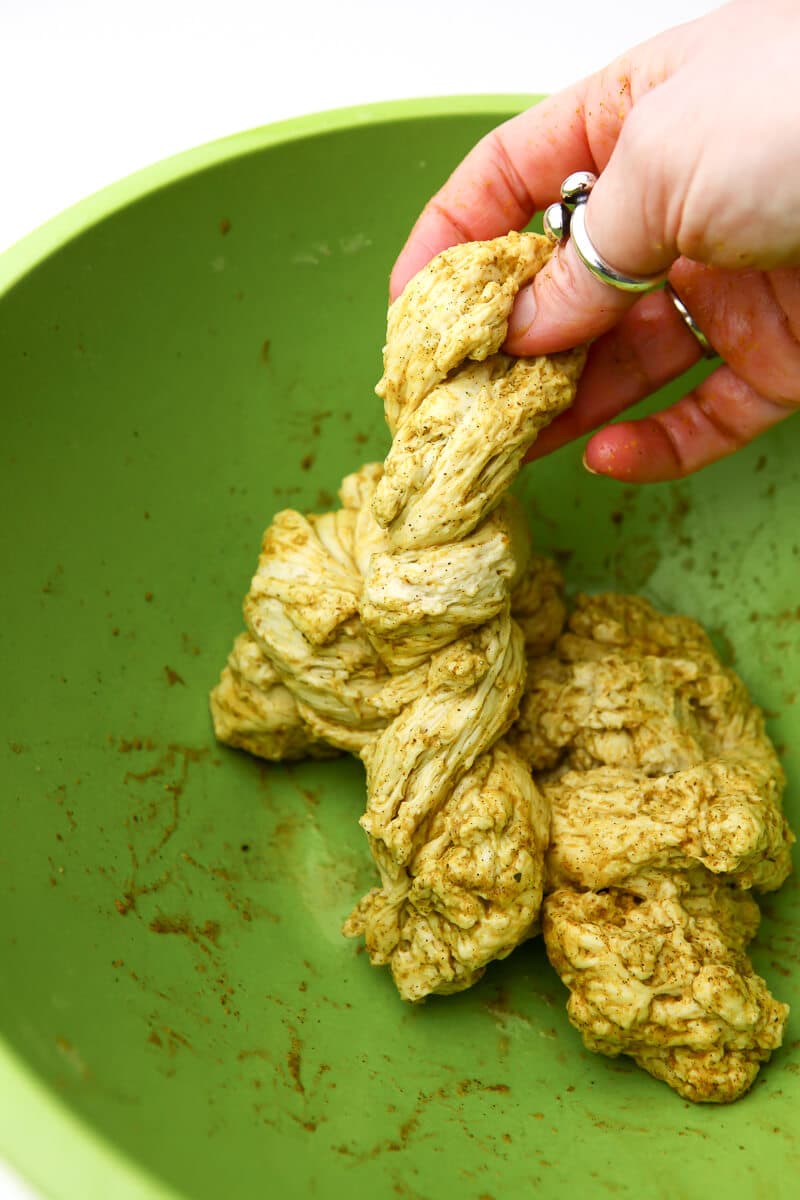 A piece of washed flour dough with spices rubbed on it being twisted with a hand.
