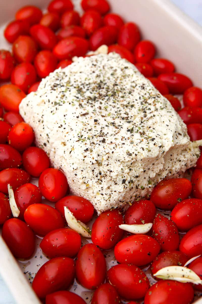 A block of tofu feta with cherry tomatoes surrounding it sprinkled with pepper and drizzled with olive oil.