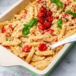 A dish of vegan baked feta with cherry tomatoes and fresh basil with a spoon scooping some out.