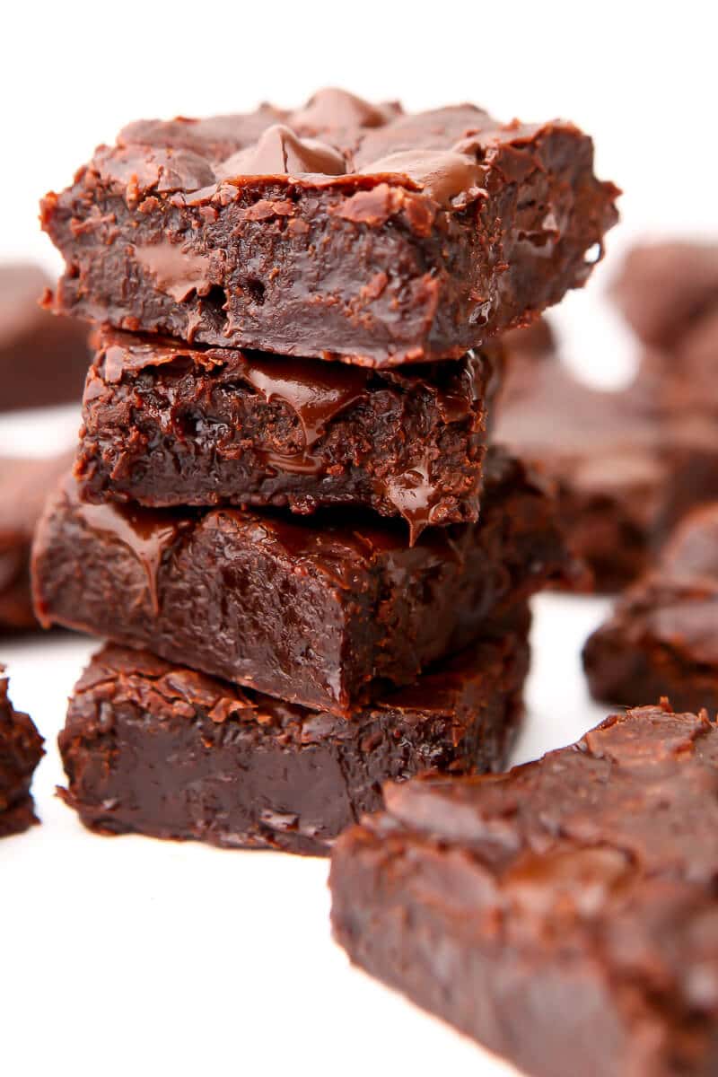 A stack of 4 vegan brownies with other brownies around it on a white surface.