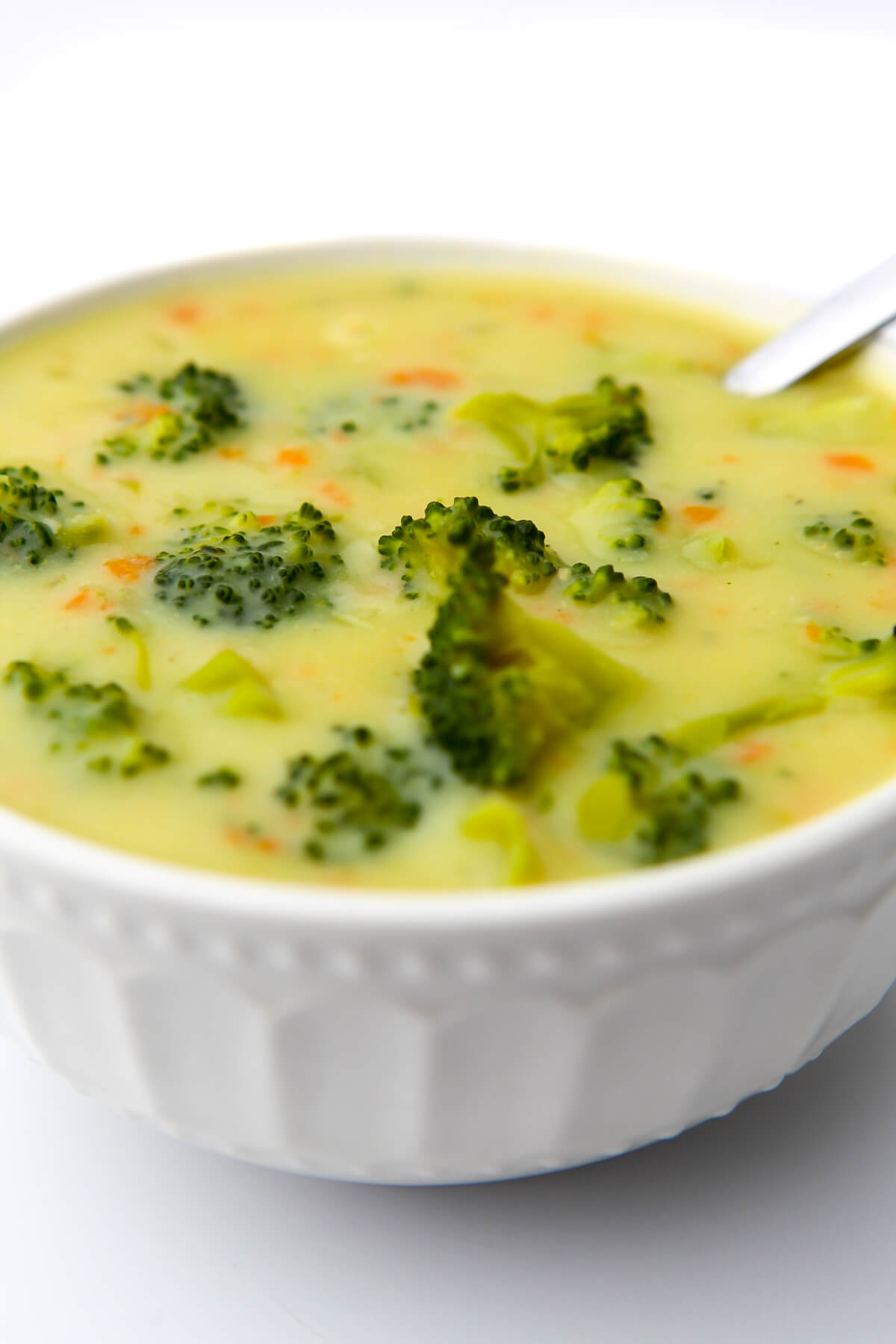 A white bowl filled with creamy vegan broccoli soup with a spoon in it.