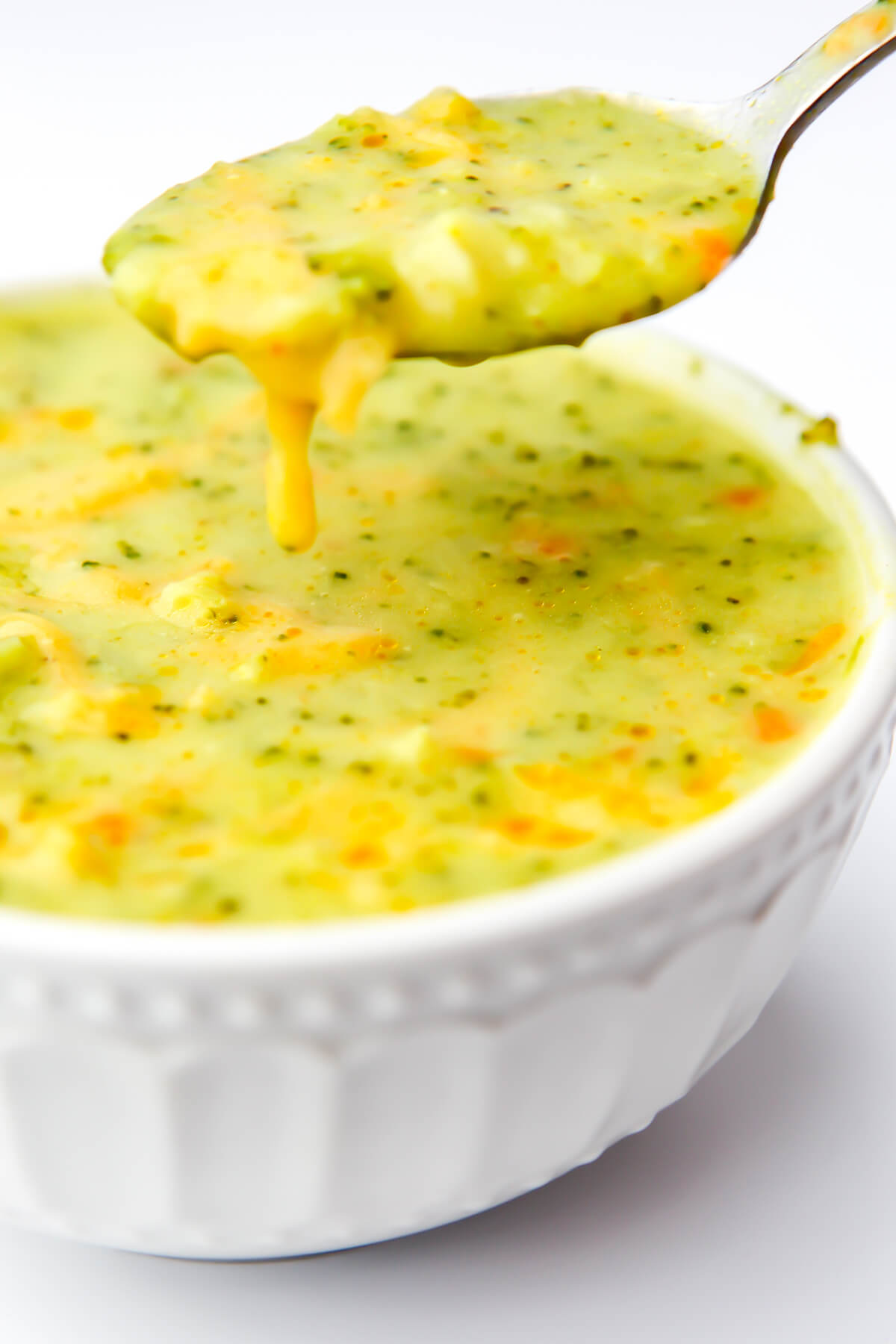 A bowl of vegan broccoli cheese soup with a spoonful of soup above it.