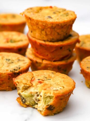 Vegan egg muffins filled with veggies stacked on a marble counter top.