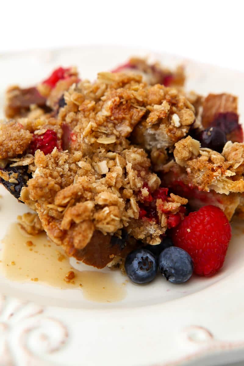 French toast casserole with berries and maple syrup served on a white plate.