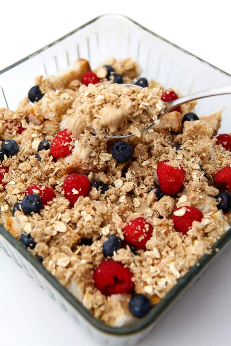 A vegan French toast casserole being sprinkled with crumble topping.