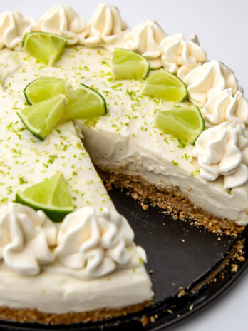 A vegan key lime cheesecake with a slice cut out of it and lime wedges on top.