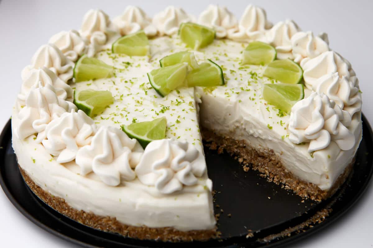 A vegan key lime cheesecake with whipped cream and lime slices on top.