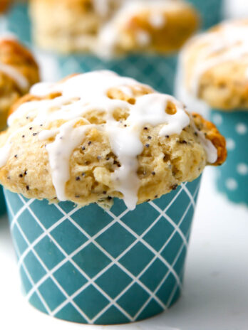 A close up of a vegan lemon poppy seed muffin with lemon drizzle on top in a blue muffin liner.
