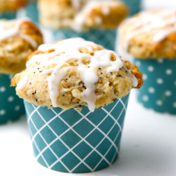 A close up of a vegan lemon poppy seed muffin with lemon drizzle on top in a blue muffin liner.