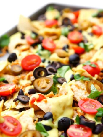 A sheet pan filled with loaded vegan nachos with homemade vegan nacho cheese, vegan taco meat, tomatoes, beans, olives and cilantro.