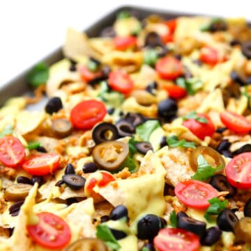 A sheet pan filled with loaded vegan nachos with homemade vegan nacho cheese, vegan taco meat, tomatoes, beans, olives and cilantro.