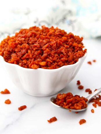 A white bowl filled with homemade bacon bits with a spoonful on the side of it.