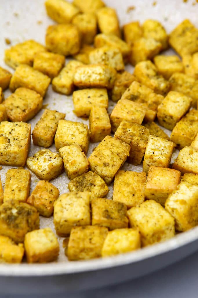 Chicken flavored tofu with poultry seasoning and nutritional yeast frying in a pan.