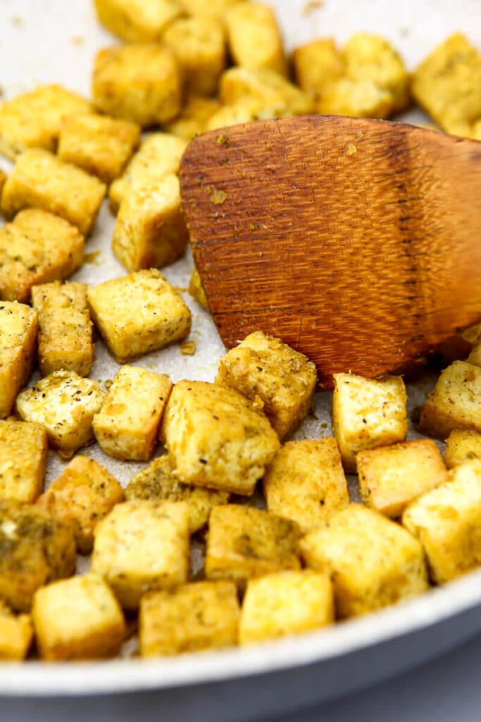 Seasoned pan fried tofu with poultry seasoning and nutritional yeast on it in frying pan.