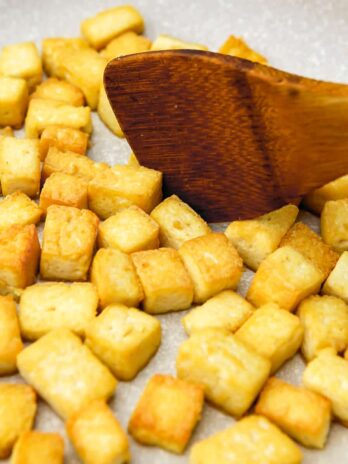 Tofu cubes frying and being stirred with a wooden spatula.