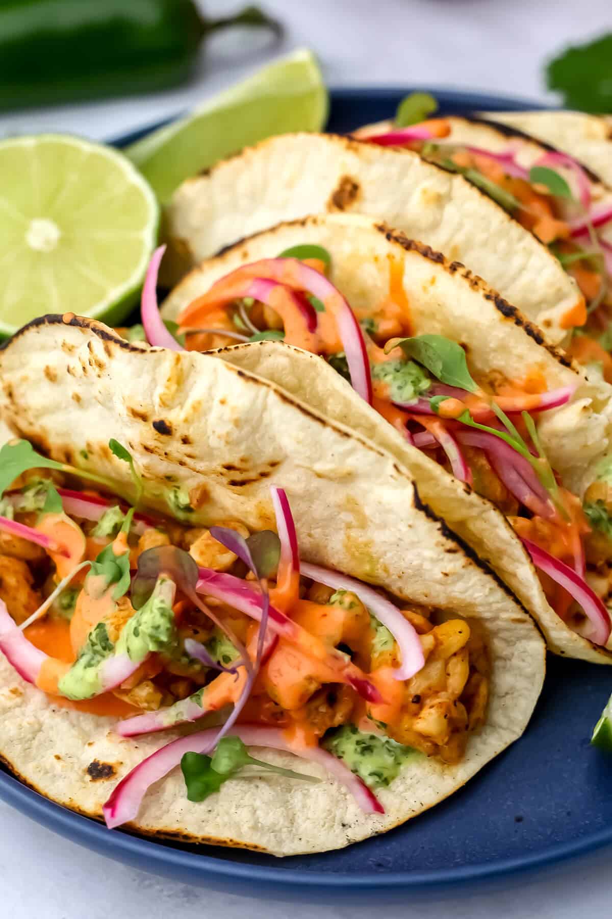A close of of tempeh tacos with Mexican pickled onions and chipotle mayo drizzled on them.