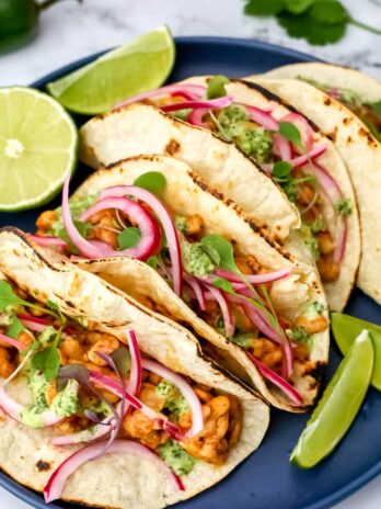 Four tempeh tacos on a blue plate with cilantro and lime slice around them.