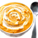 A bowl of vegan butternut squash soup with vegan sour cream swirled into it.