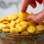 A bowl of vegan cheez-Its style crackers with a hand picking one up.
