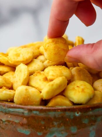 A bowl of vegan cheez-Its style crackers with a hand picking one up.