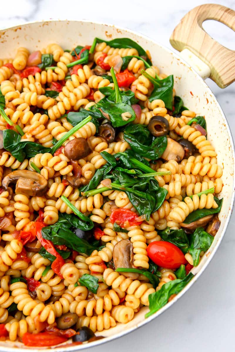 A top view of a pan filled with a Mediterranean pasta  salad filled with tomatoes, mushrooms, onions, and spinach tossed in a balsamic reduction.
