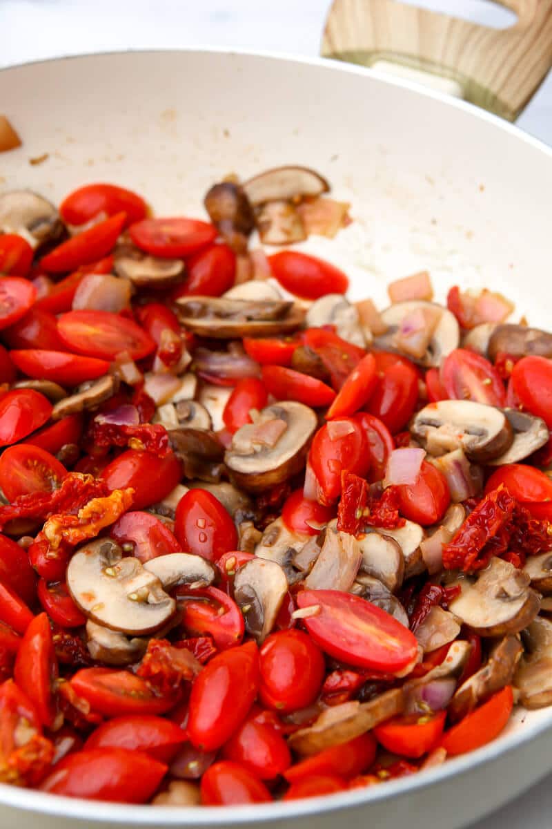 Onions, mushrooms, and tomatoes sautéing in a pan to make a veggie pasta salad.