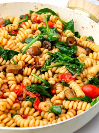 A large pot filled with vegan pasta salad with veggies and a balsamic sauce.