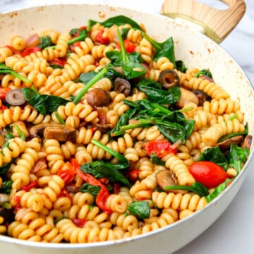 A large pot filled with vegan pasta salad with veggies and a balsamic sauce.
