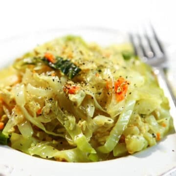 A white plate with vegan haluski made with cabbage and noodles with a fork on the side.