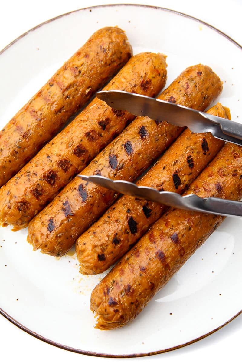Five vegan Italian sausages on a white plate after they have been grilled.