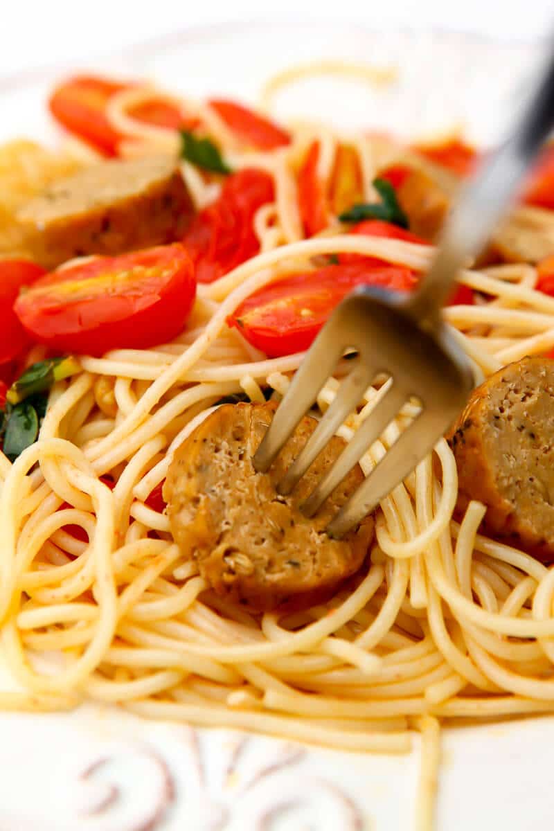 A plate of spaghetti with tomatoes and slices of vegan Italian sausages. 
