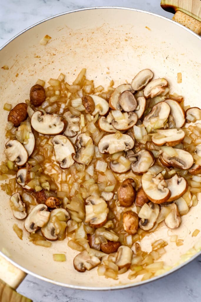 Onions and mushrooms frying in a large pan to make vegan stroganoff.