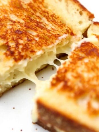 A vegan grilled cheese sandwich that is being pulled apart to show the melted cheese inside.