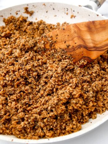 A white skillet filled with homemade vegan ground beef being stirred with a wooden spoon.